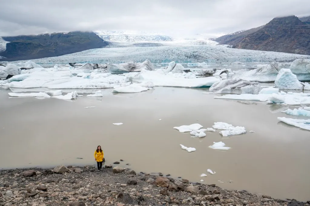 kate storm in a yellow jacket standing at the edge of fjallsarlon glacier lagoon