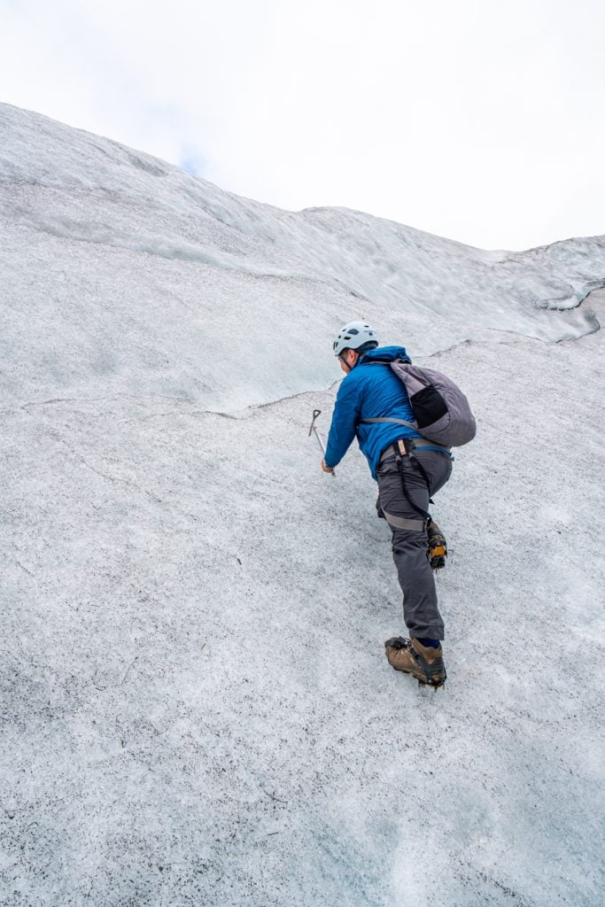 jeremy storm in a blue jacket posing on a glacier in iceland like he's ice climbing