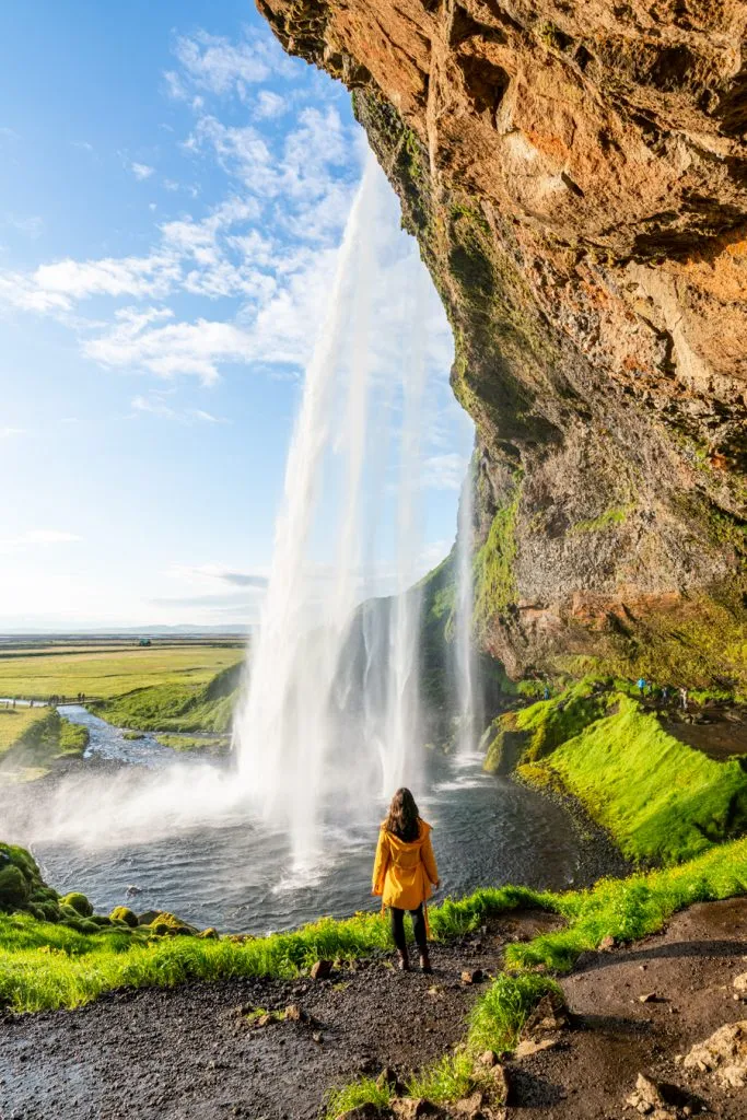 kate storm in a yellow jacket in front of seljalandsfoss fun stop plan a trip to iceland
