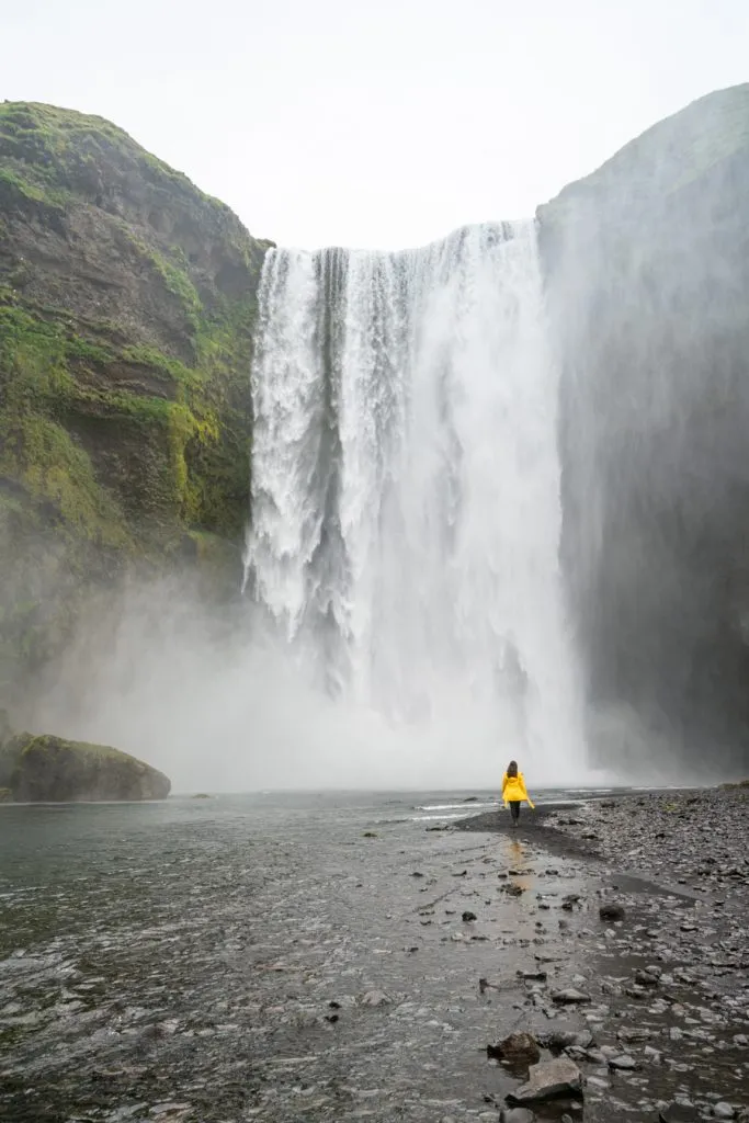 kate storm in a yellow jacket in front of skogafoss one of the best things to do in iceland