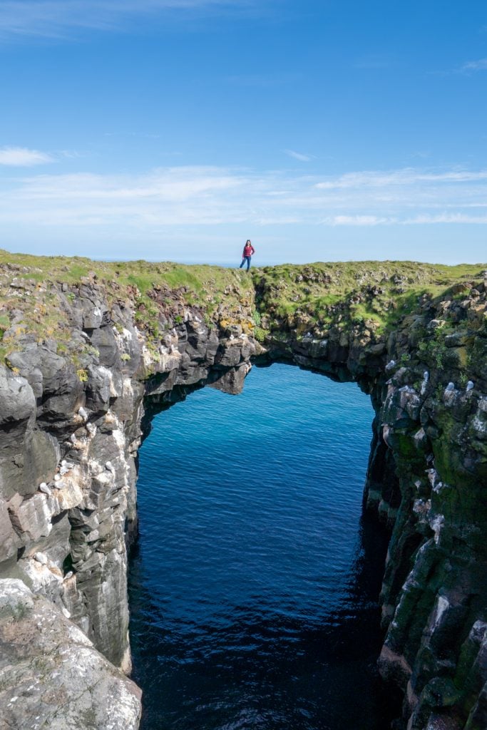 kate storm walking over an arch over the water arnarstapi