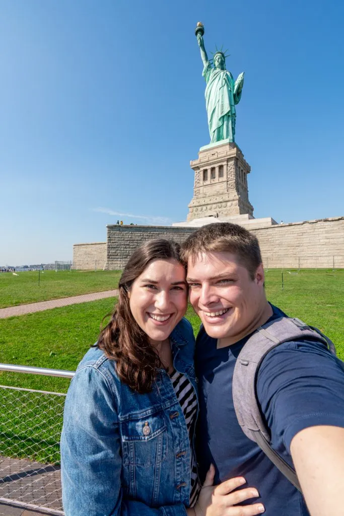 kate storm and jeremy storm taking a selfie with the statue of liberty nyc