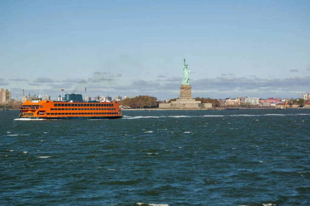 orange staten island ferry passing by liberty island in new york harbor