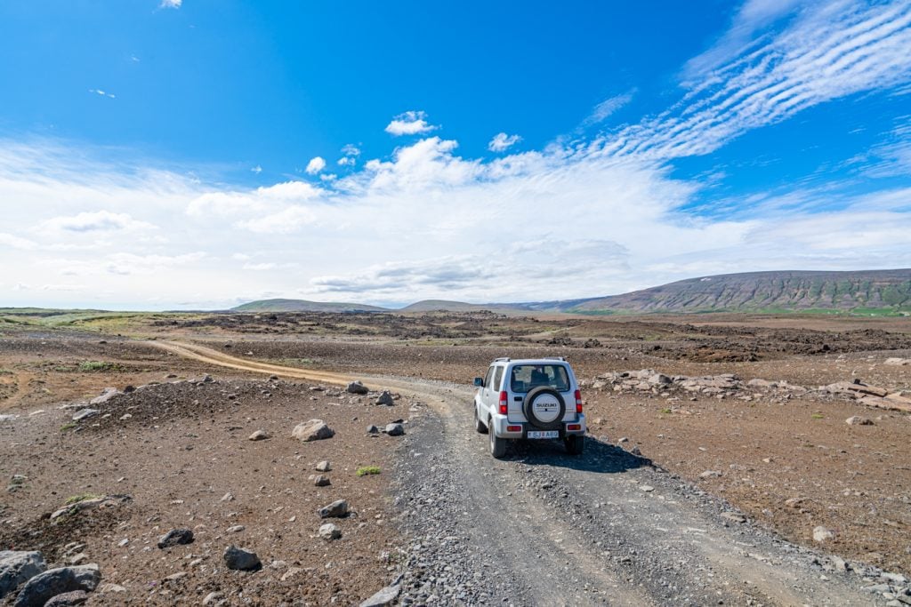 gray jeep on an empty dirt road iceland, under blue skies