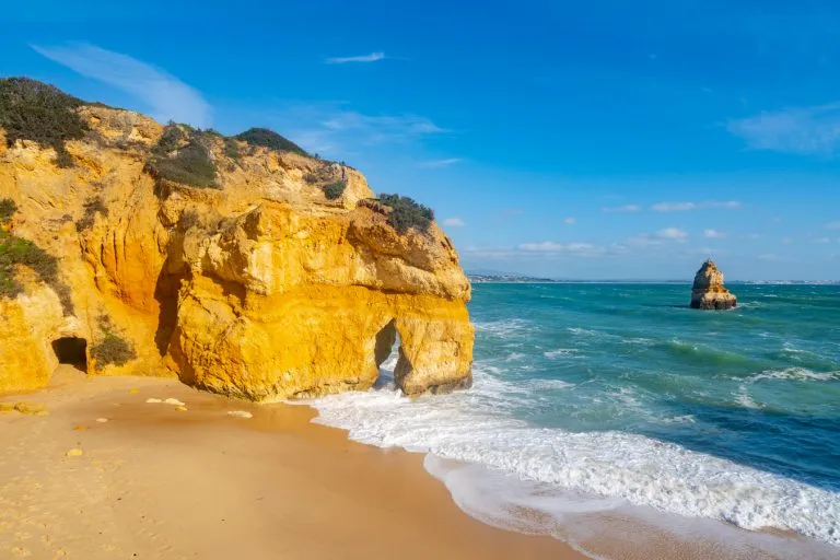 close up of rock formations and golden sand on the praia do camilo in algarve portugal, one of the best places to visit on a 2 weeks in spain and portugal itinerary
