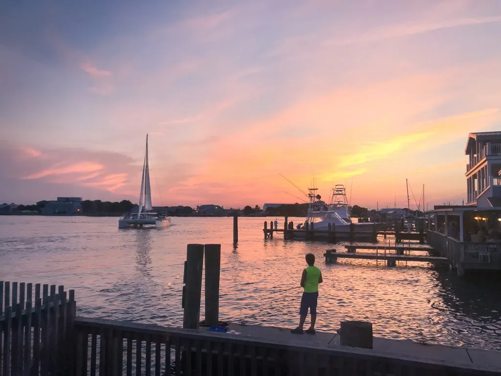 person standing on a dock at sunset watching a sailboat one of the best activities emerald isle nc