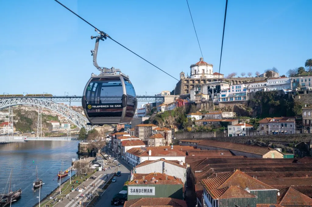 view of cable car in front of bridge and monastery in porto, a cool experience during an itinerary for spain and portugal in 2 weeks