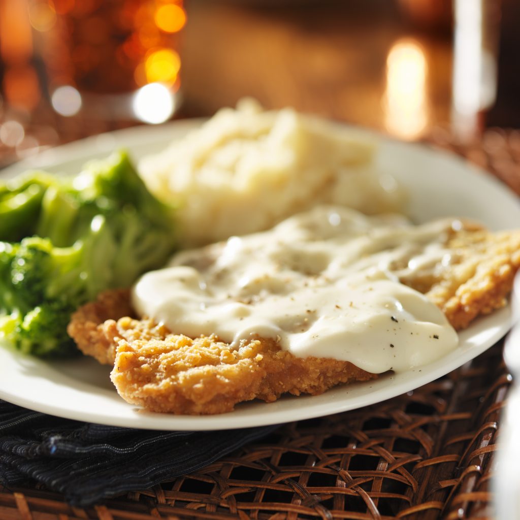 chicken fried steak dinner with gravy on top on a white plate