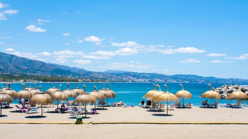 beach with straw umbrellas on puerto banus spain