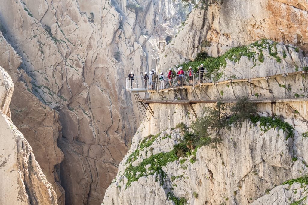 group of people with helmets hiking along a gorge el caminito del rey