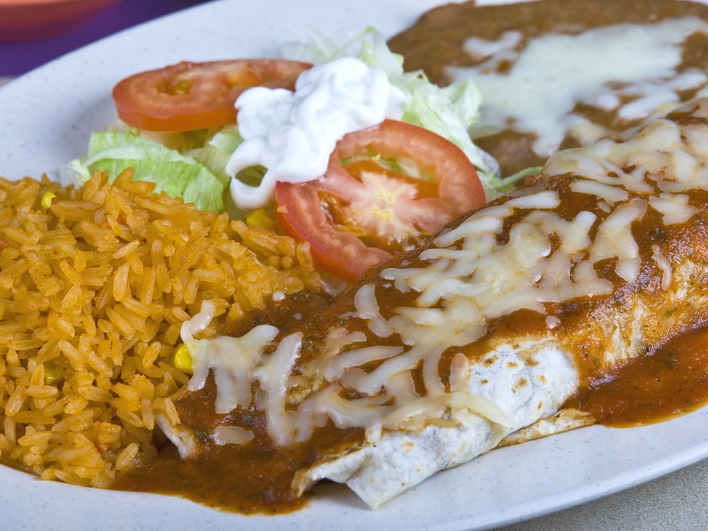 texmex style burrito served on a white plate with rice and beans