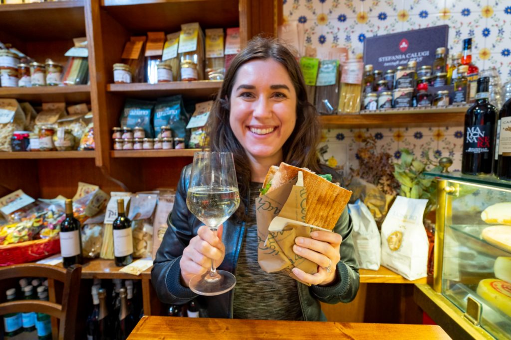kate storm holding up a panino and wine in a shop in florence when eating in italy