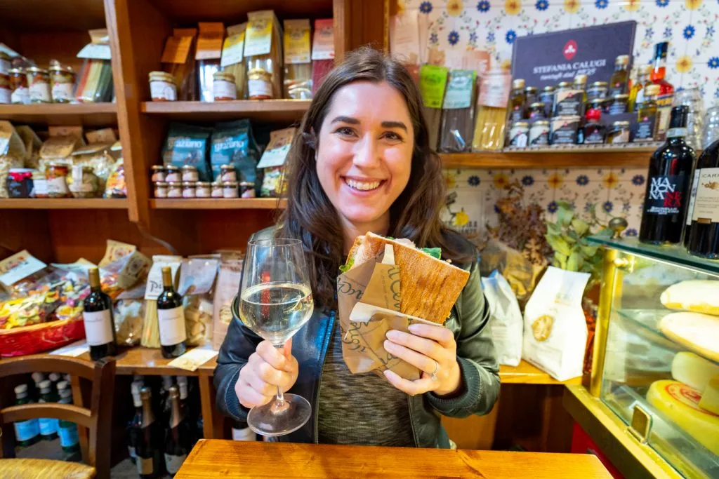 kate storm holding up a panino and wine in a shop in florence when eating in italy
