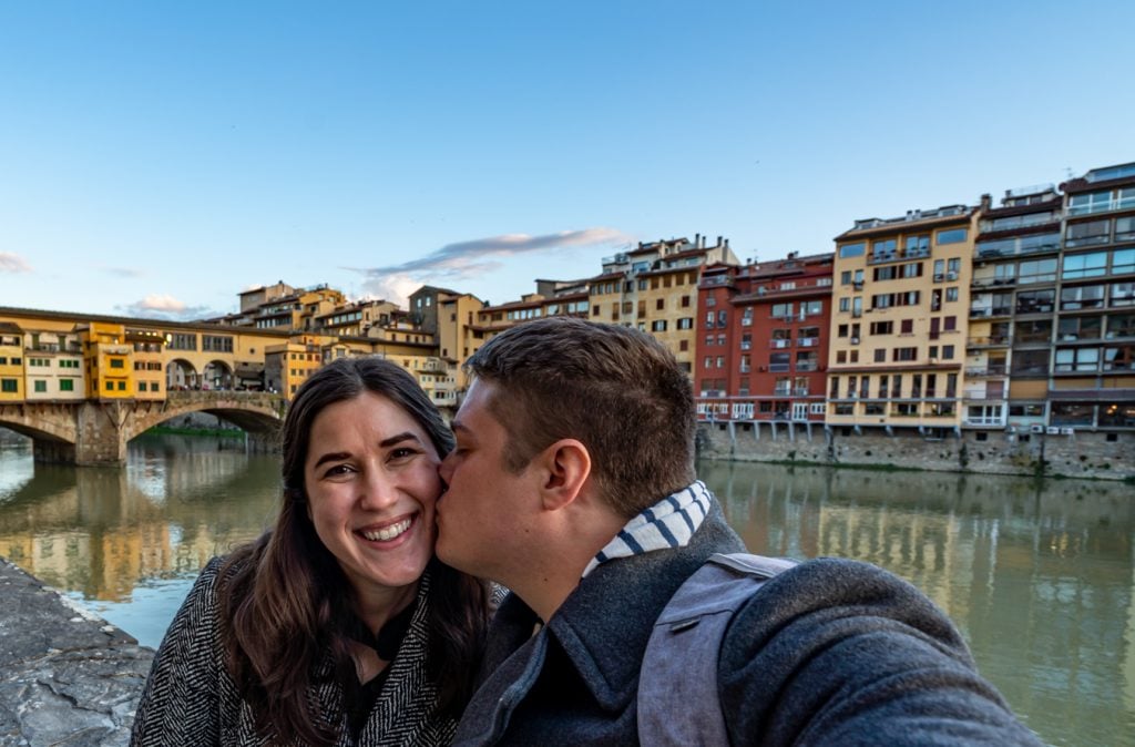 kate storm and jeremy storm sitting on the edge of the arno with the ponte vecchio in the background