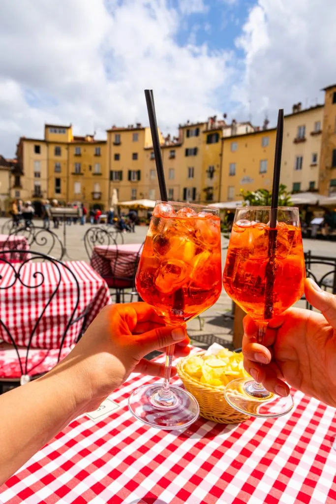 2 aperol spritzes being held up in lucca, a fun stop during a 14 days in italy itinerary