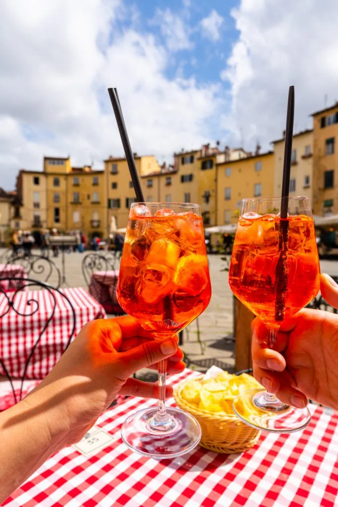 two aperol spritzes being held up before a meal in lucca, charged italy coperto cover charge