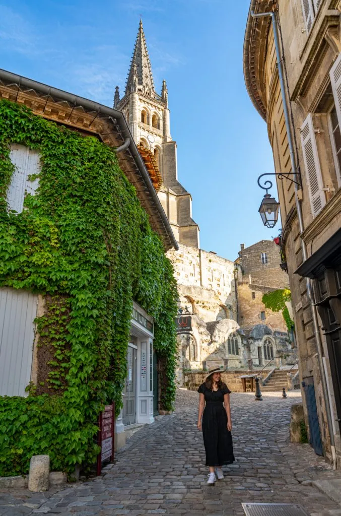 kate storm in a black dress walking down a cobblestone street in medieval st emilion