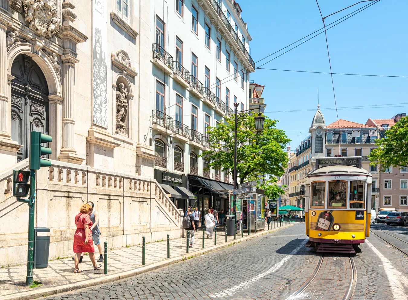 view of a yellow tram approaching the camera next to a church in lisbon, one of the many typical views to look forward to when planning a trip to portugal
