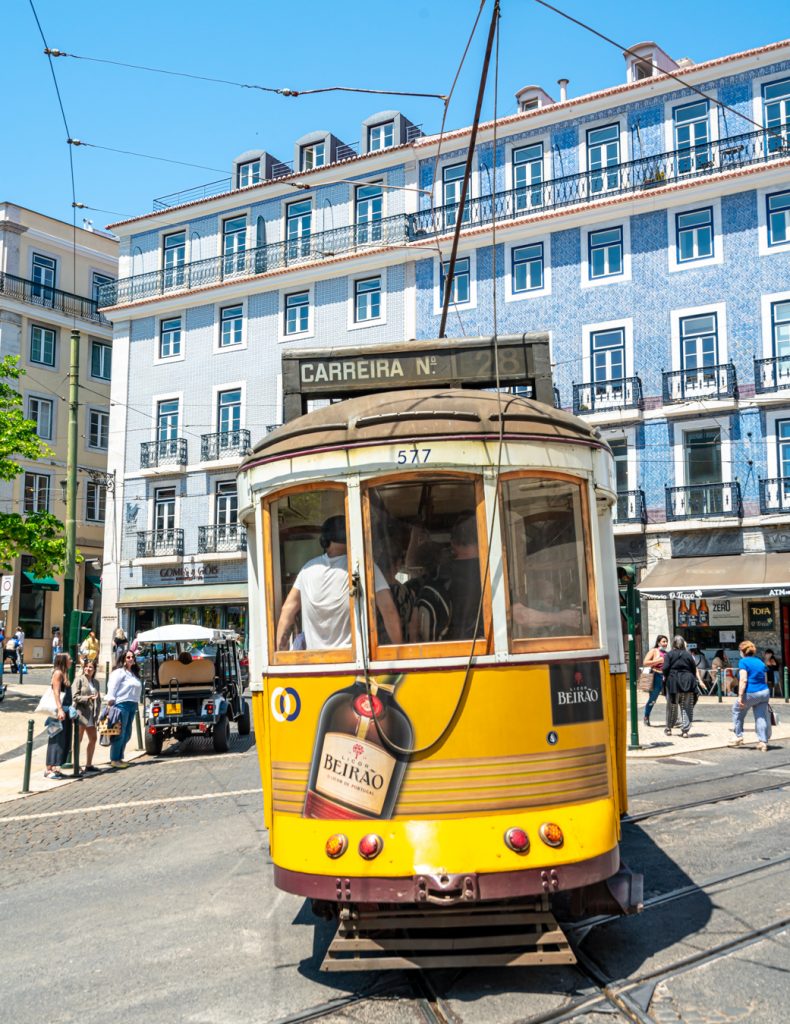 yellow tram approaching in chiado lisbon with blue building behind it