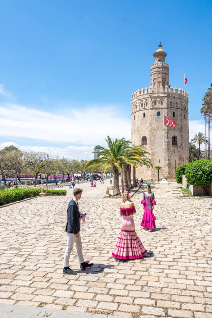 view of the torre del oro with women in flameno dresses in front, a fun place to walk during a one day seville itinerary