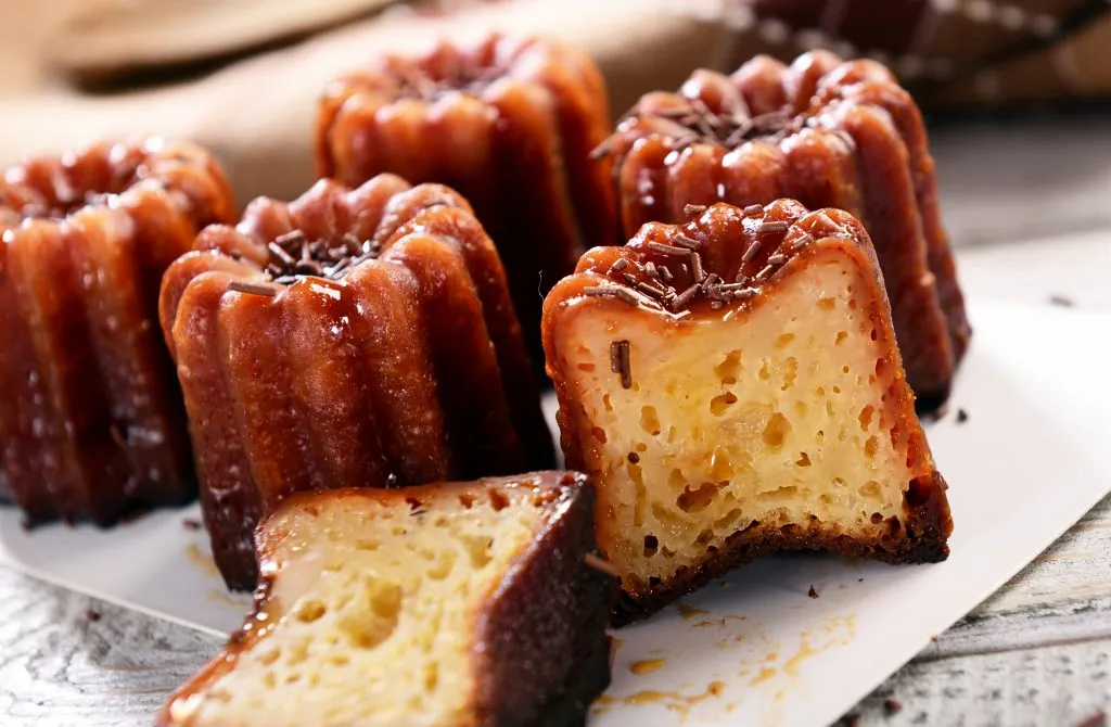 several caneles de bordeaux on a white paper, one is sliced in half