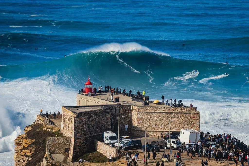 view of people watching a surfer riding enormous wave in nazare portugal road trip itinerary