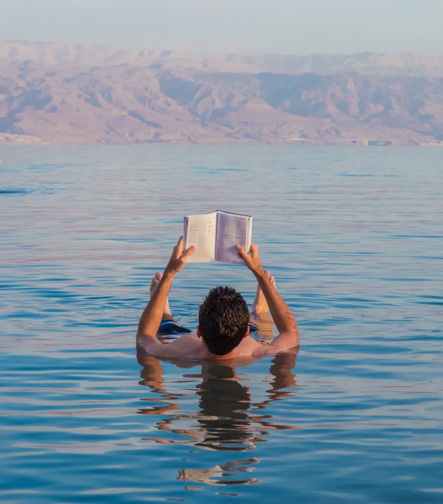 man floating in dead sea jordan while holding up a book
