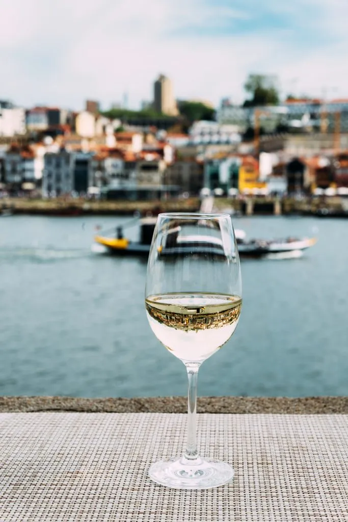 glass of white wine sitting on the edge of the river in porto portugal