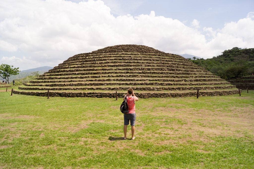 man standing in front of Guachimontones pyramid to take a picture