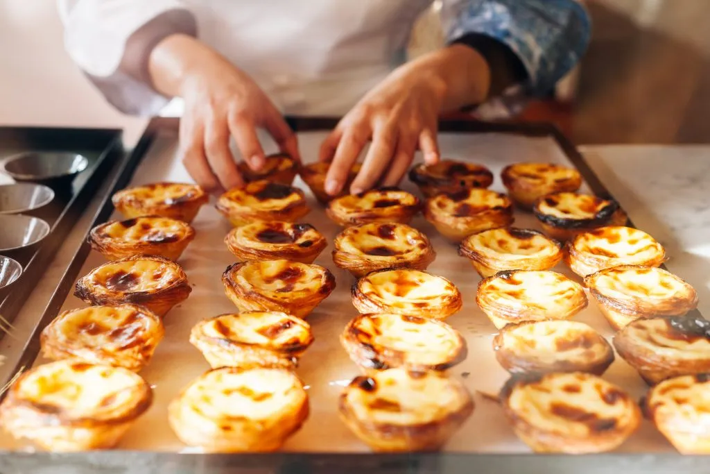 person arranging pasteis de nata on a tray, one of the best things to buy in portugal