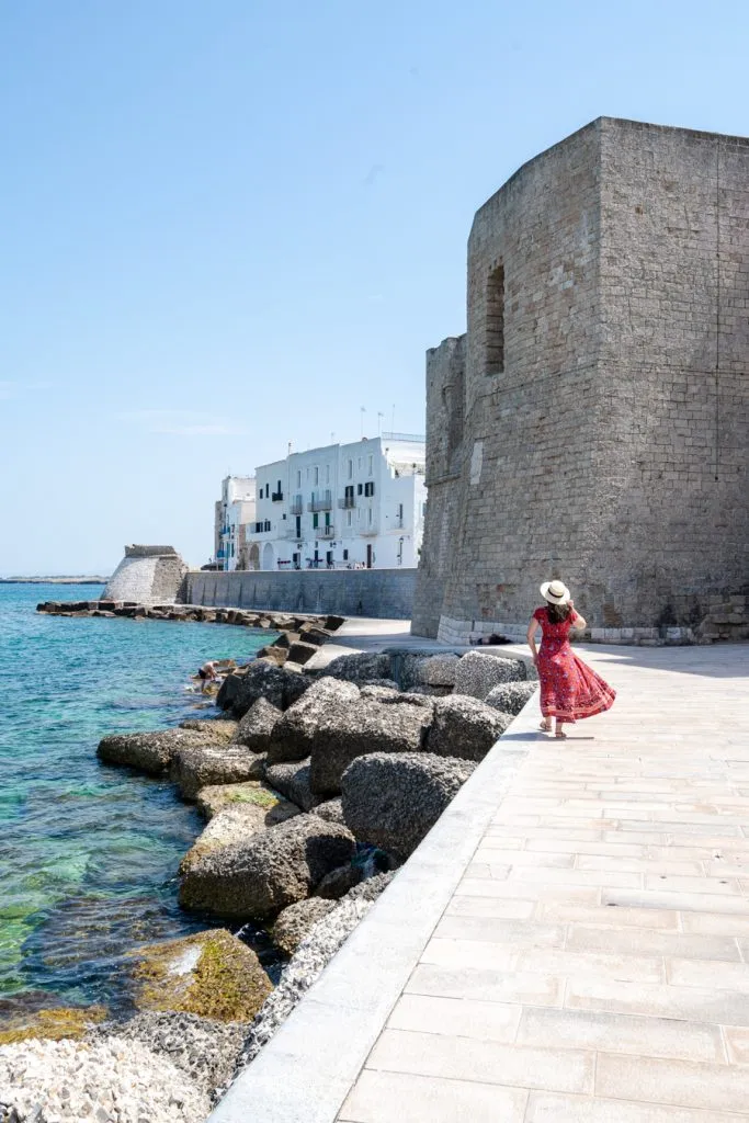 kate storm in a red dress walking along the lungomare of monopoli, one of the best puglia towns to visit