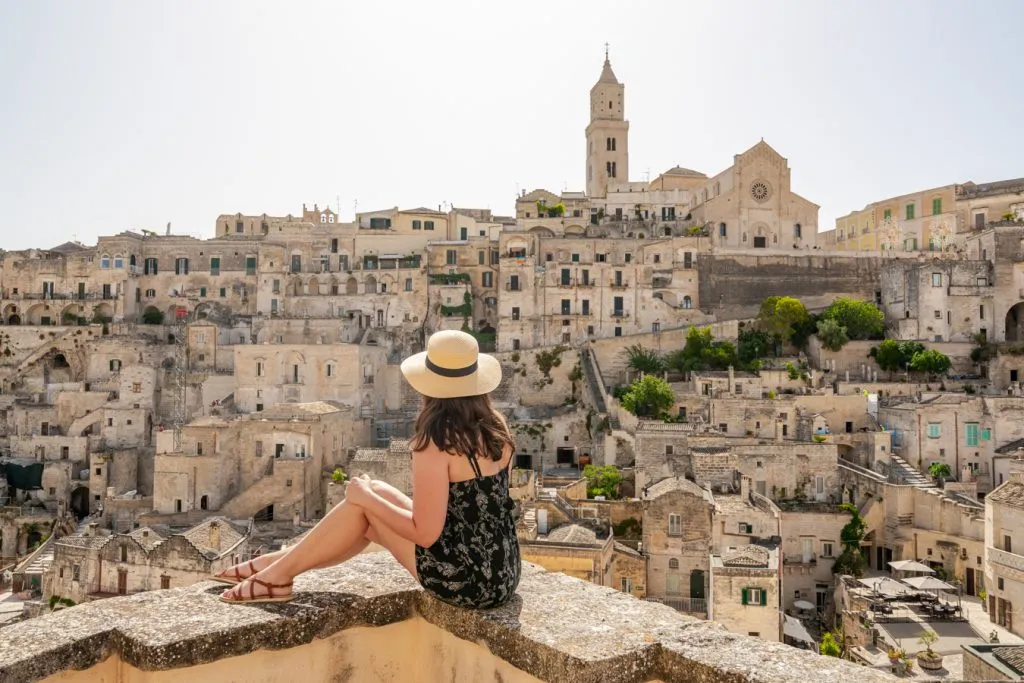 kate storm sitting on the edge of a balcony on matera in summer--visiting matera in july can be considered a bit of an italy travel mistake