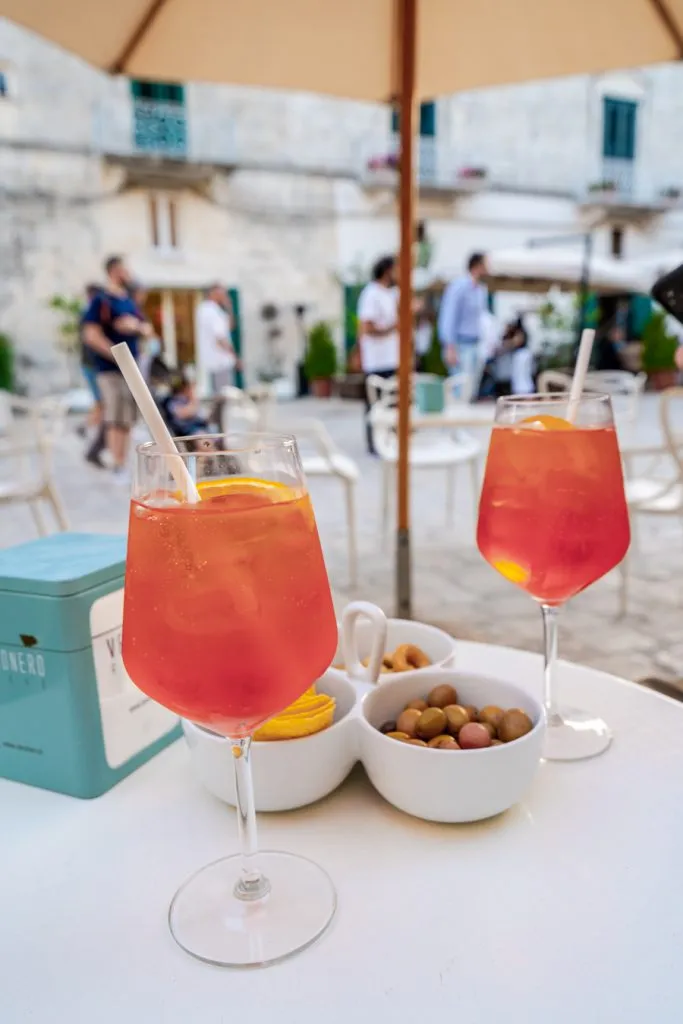 2 aperol spritzes with snacks on a table in a piazza in matera italy southern road trip