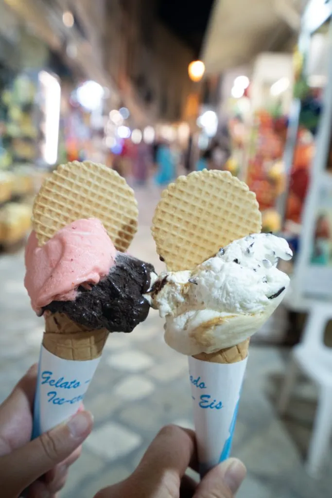 two servings of gelato being held in front of a shop in otranto puglia at night