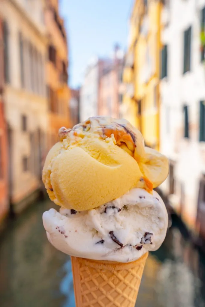 two scoops of gelato in a cone in front of venice canal--skipping gelato is definitely on the list of what not to do in italy