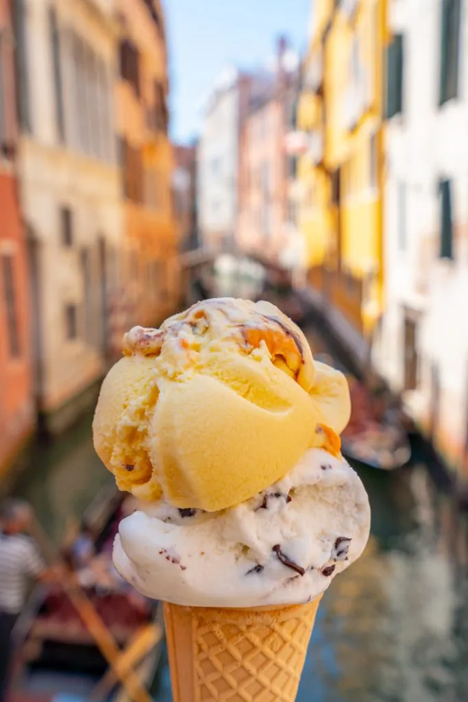two scoops of gelato being held in front of a canal during venice summer