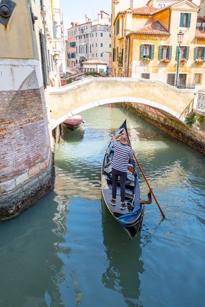 gondolier navigating a boat through a bridge during summer venice italy