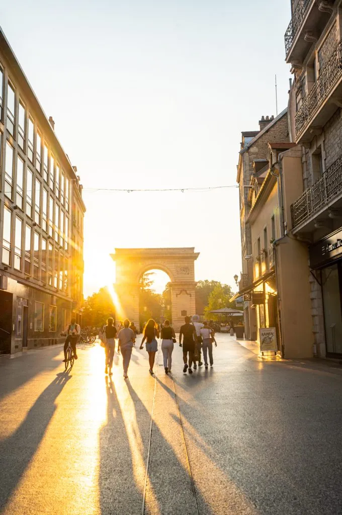 people walking down rue de la liberte at sunset with arch in the distance