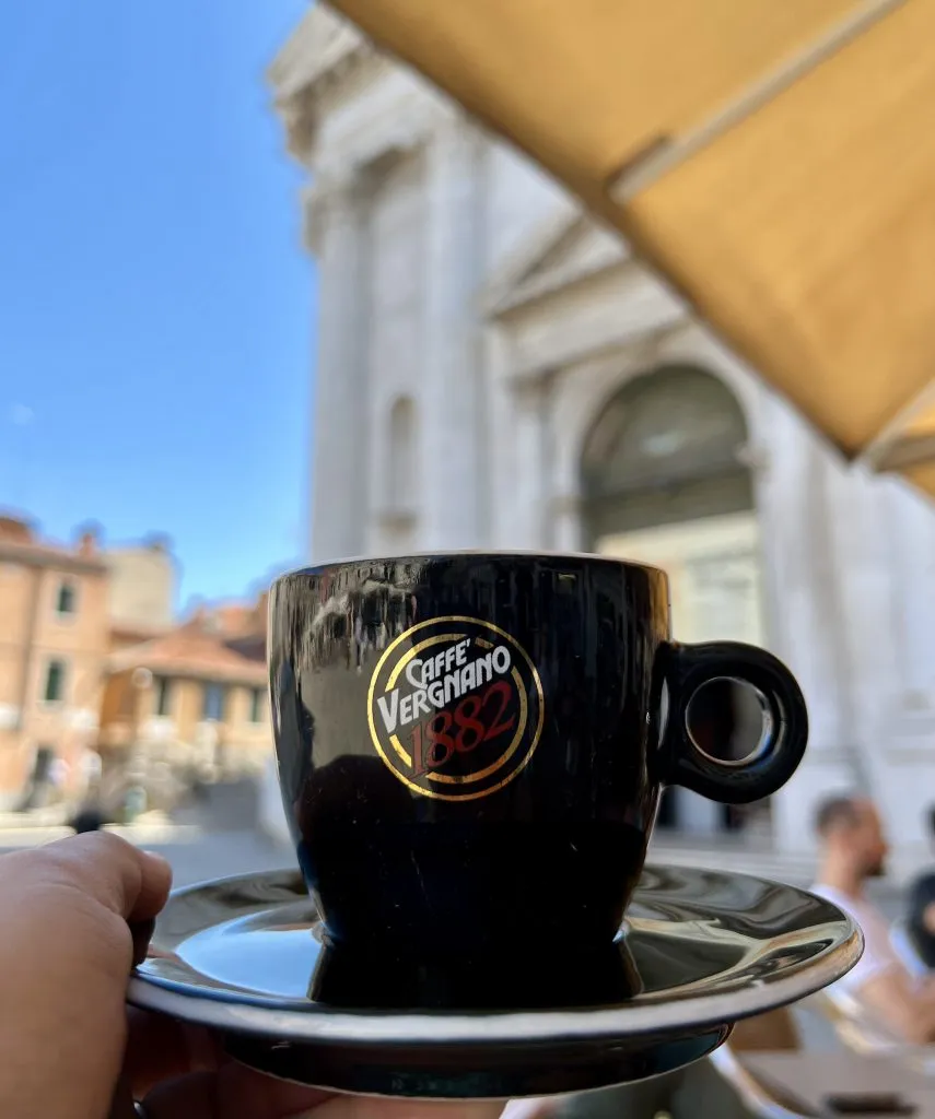 black cup of italian coffee being held up in piazza san barnaba venice