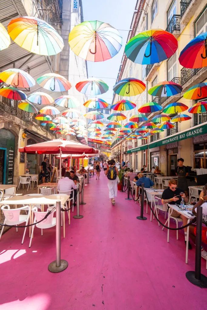 pink street in lisbon portugal with umbrellas hanging overhead