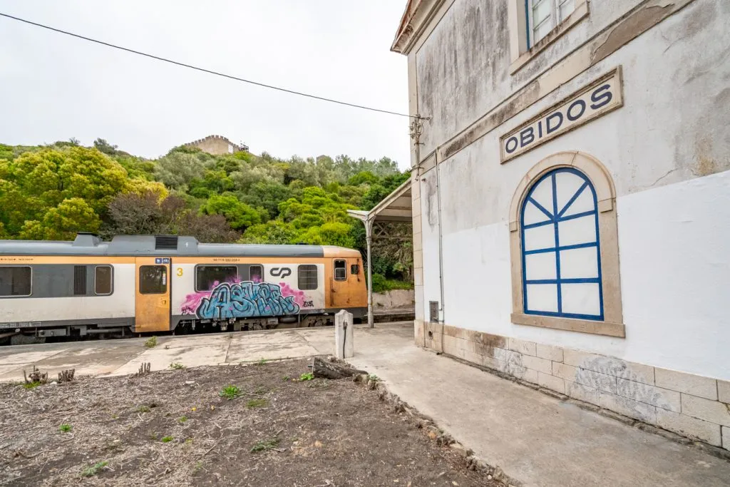 obidos train station with a graffitied train pulling into the station