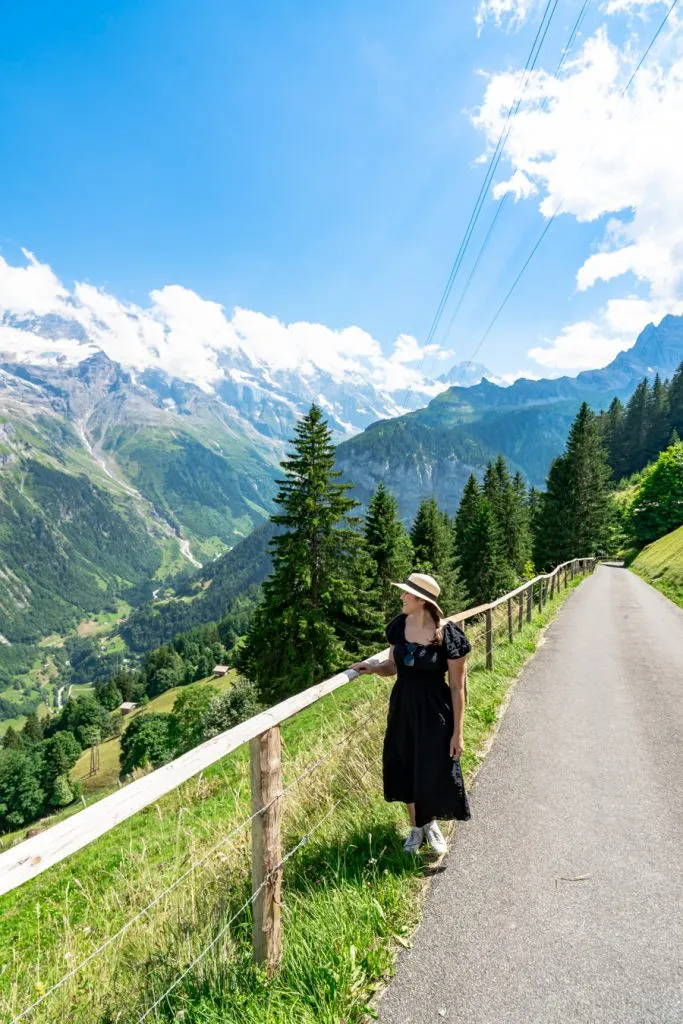 kate storm in a black dress with the alps in the background on the murren to gimmelwald hike