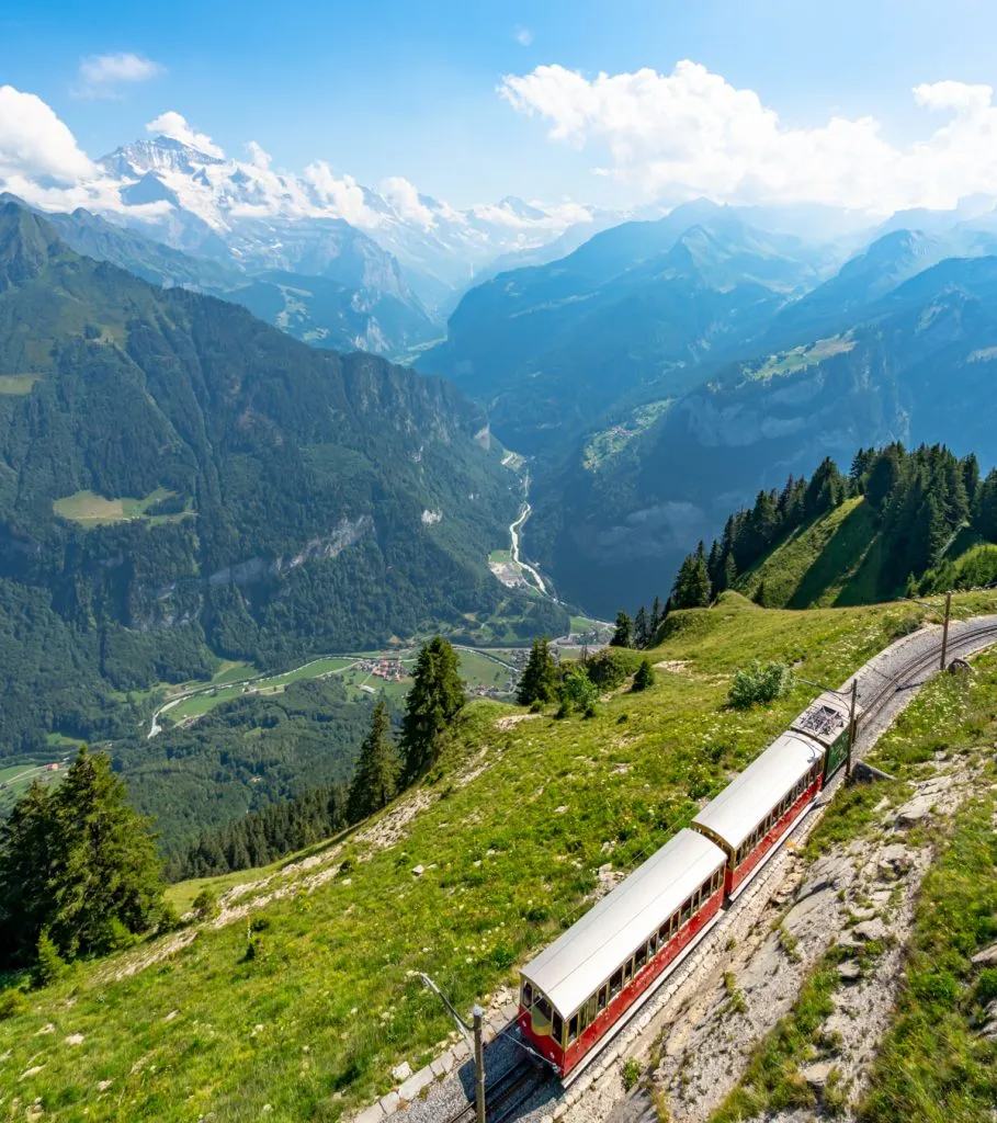 historic red cogwheel train approaching schynige platte with alps in the background, one of the most beautiful places in switzerland vacation
