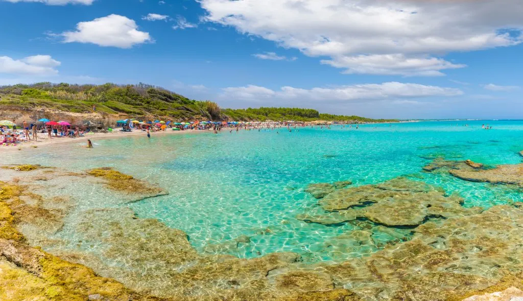 baia dei turchi with water in the foreground and beachgoers in the background