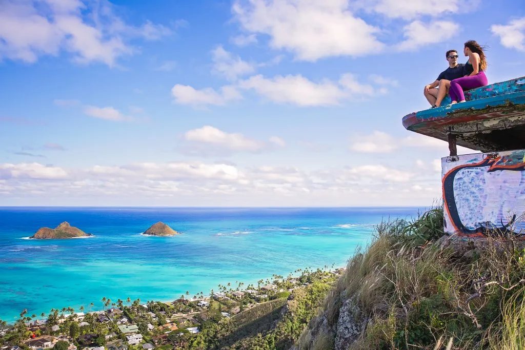 couple sitting at the summit of the lanikai pillbox hike with ocean in the distance