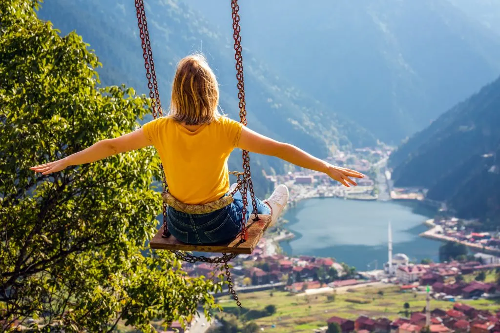 woman on a yellow shirt swinging above the mountains and village of trabzon, one of the most beautiful places in turkey to visit