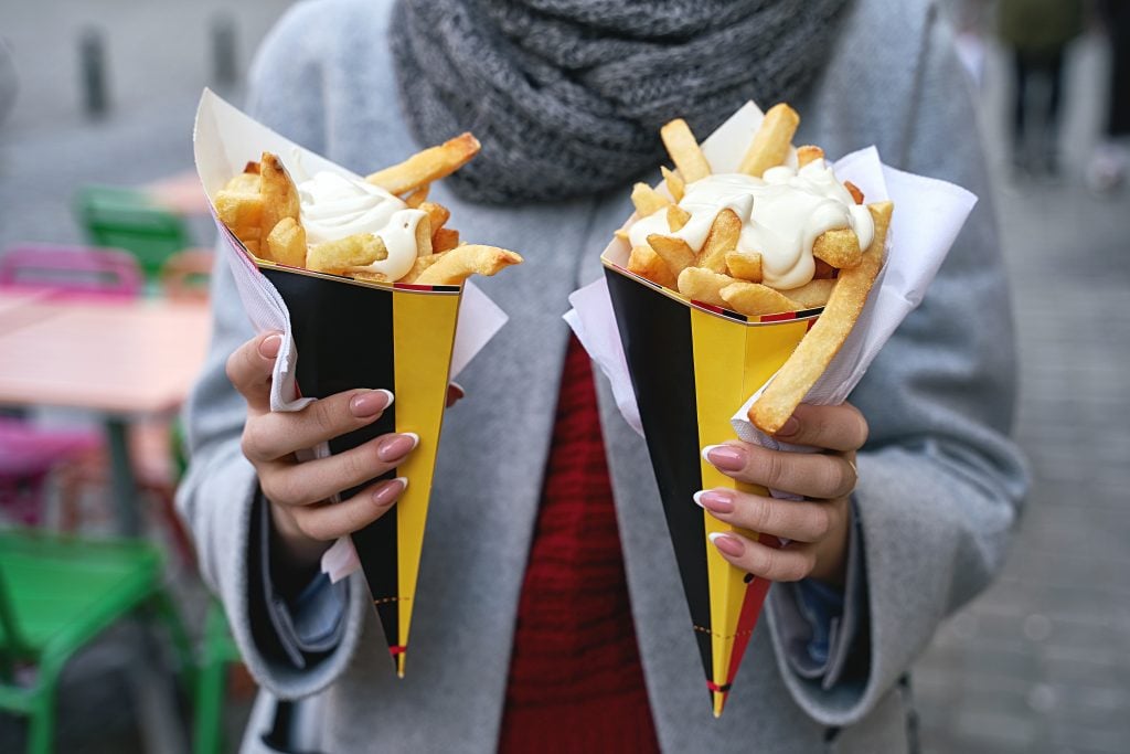 woman holding 2 cones of belgian frites topped with mayo