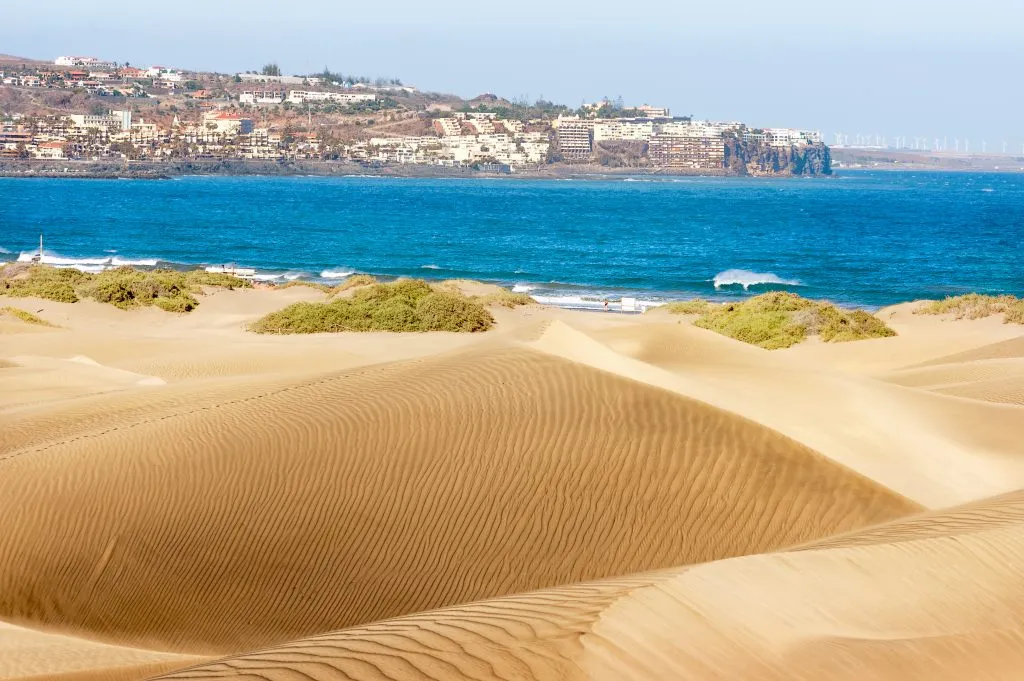 sand dunes with water visible in the background in maspalomas, one of the best beach towns in spain