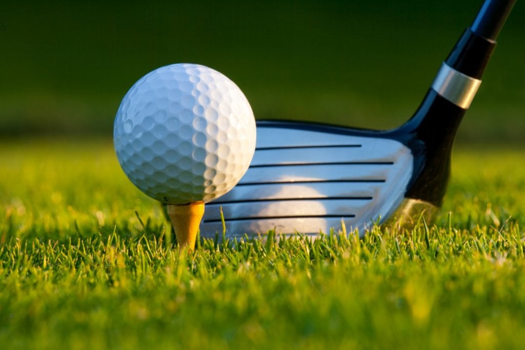 golf ball on a tee with a club situated behind it