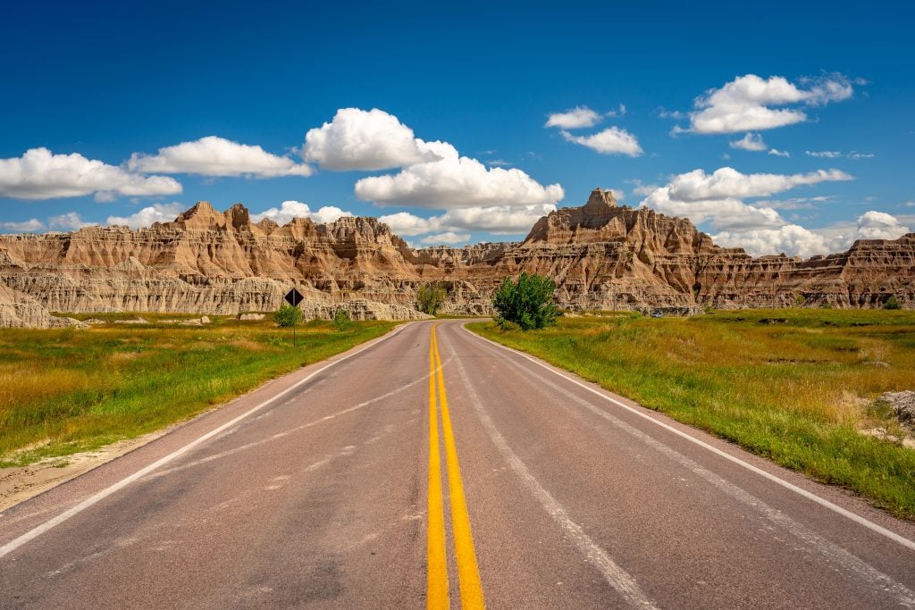 straight 2 lane road leading through the landscape of badlands national park, one of the best road trips midwest usa
